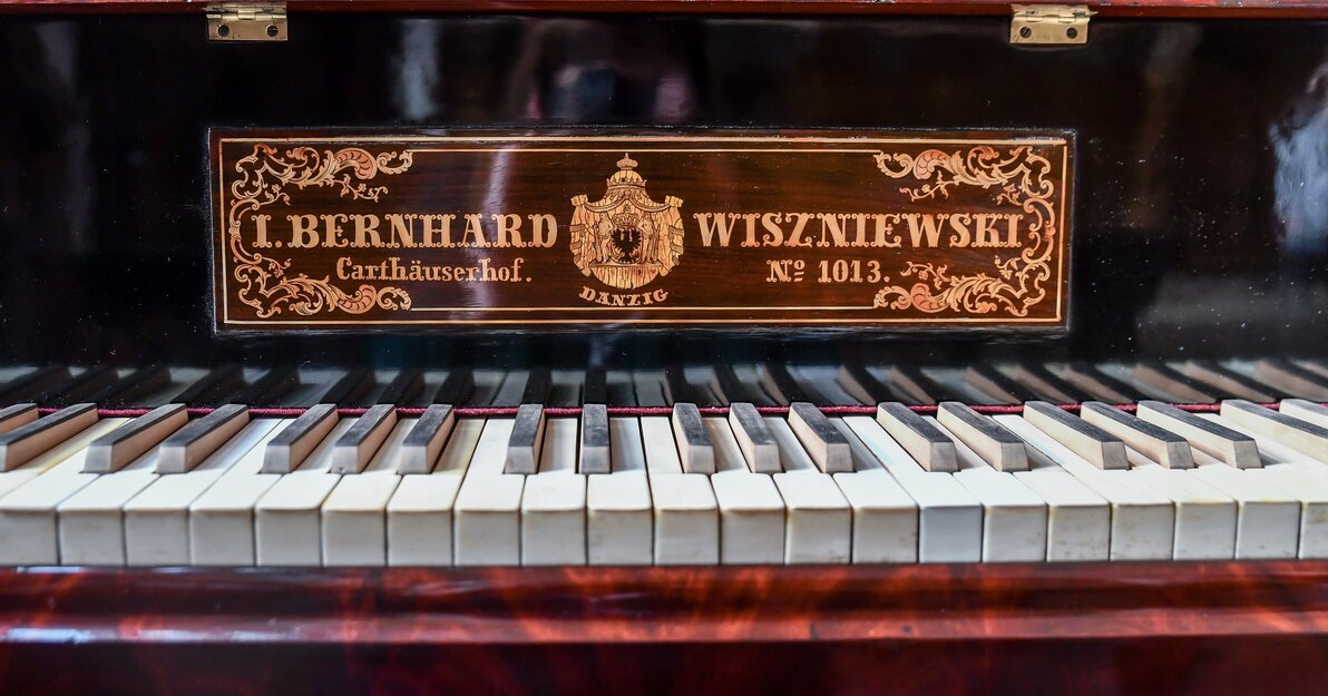 Zdjęcie przedstawia klawiaturę najstarszego gdańskiego fortepianu z około 1830 roku. Nad klawiaturą znajduje się tabliczka znamionowa firmy Wiszniewskich w języku niemieckim: I. Bernhardt Wiszniewski, Carthauserhof, no 1013.