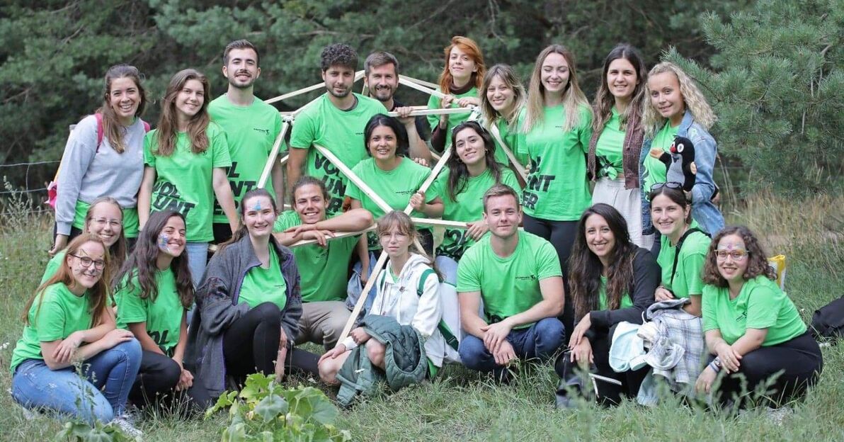 Wolontariusze w zielonych koszulkach "Europejskiej Stolicy Wolontariatu" w parku. W tle drzewa
