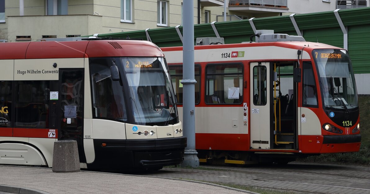 Na zdjęciu dwa tramwaje, w tle blok mieszkalny. 