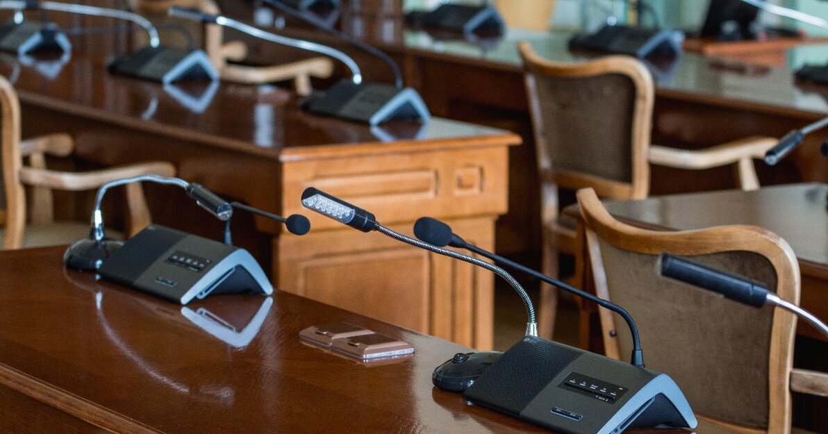 Pusta sala obrad Rady Miasta Gdańska widziana z perspektywy stołów, na których znajdują się mikrofony i urządzenia do głosowania.