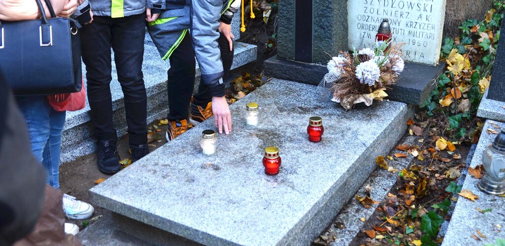 Zdjęcie. Uporządkowany nagrobek ze zniczami. W kadrze - lewym rogu ludzie. 