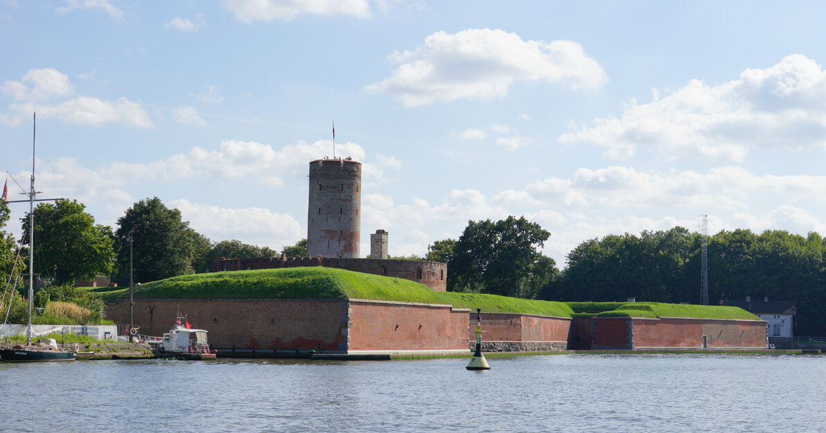 Zdjęcie przedstawia jeden z bastionów Twierdzy widoczny od strony otaczającego ją kanału wodnego. W tle widoczna wieża.