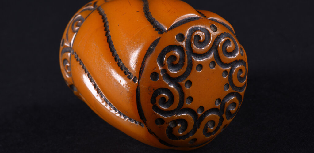 Gałka do laski w formie obłego, lekko zwężającego się ku dołowi walca, o dwóch podstawach w formie koła. Gałka rozczłonkowana po obwodzie przez esowate linie utworzone przez gęsto ułożone kropki. Górna podstawa dekorowana w koło ornamentem pojedynczych, połączonych ze sobą spirali, przy łączeniu ujętych po bokach dwoma kropkami. Dolna partia gałki dekorowana wąskim fryzem z ornamentem tworzonym przez szereg pojedynczych spirali w półłuku, między półłukami pojedyncza kropka.