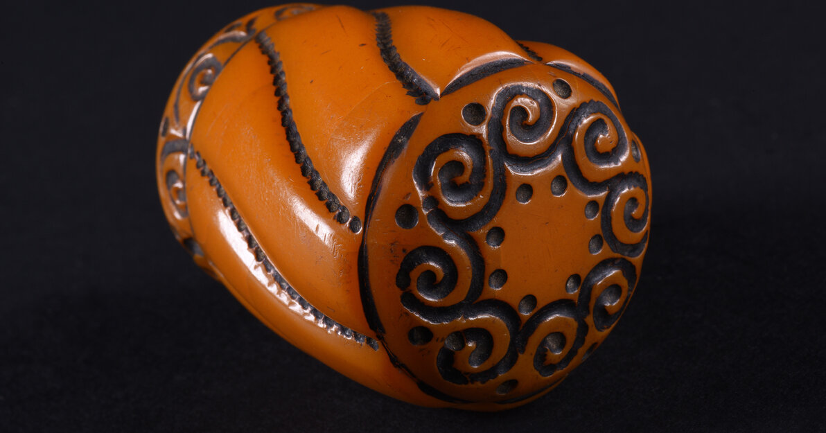 Gałka do laski w formie obłego, lekko zwężającego się ku dołowi walca, o dwóch podstawach w formie koła. Gałka rozczłonkowana po obwodzie przez esowate linie utworzone przez gęsto ułożone kropki. Górna podstawa dekorowana w koło ornamentem pojedynczych, połączonych ze sobą spirali, przy łączeniu ujętych po bokach dwoma kropkami. Dolna partia gałki dekorowana wąskim fryzem z ornamentem tworzonym przez szereg pojedynczych spirali w półłuku, między półłukami pojedyncza kropka.